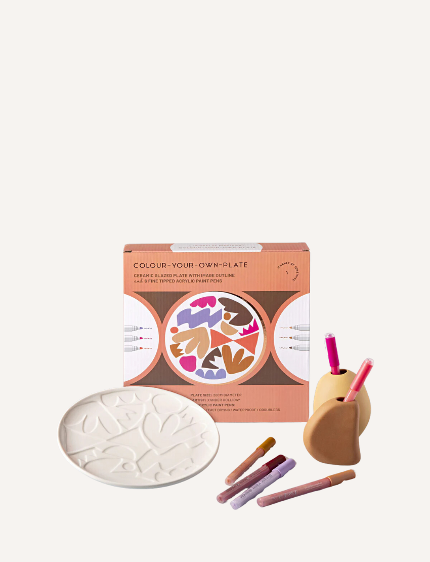 Image of the "Paint Your Own Plate - J.O.S Studio" by Journey of Something. The kit includes a plain ceramic plate with embossed leaf patterns, a set of colored markers, and a small palette. The packaging displays a partially colored plate as an example of the potential outcome.