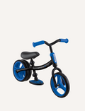 The Globber Go Bike Duo Balance Bike is a small, black and red toddler bike with no pedals, featuring EVA foam wheels. It has a black frame, a red adjustable handlebar, a black seat, and red wheels. The bike also includes a small footrest platform on the frame.