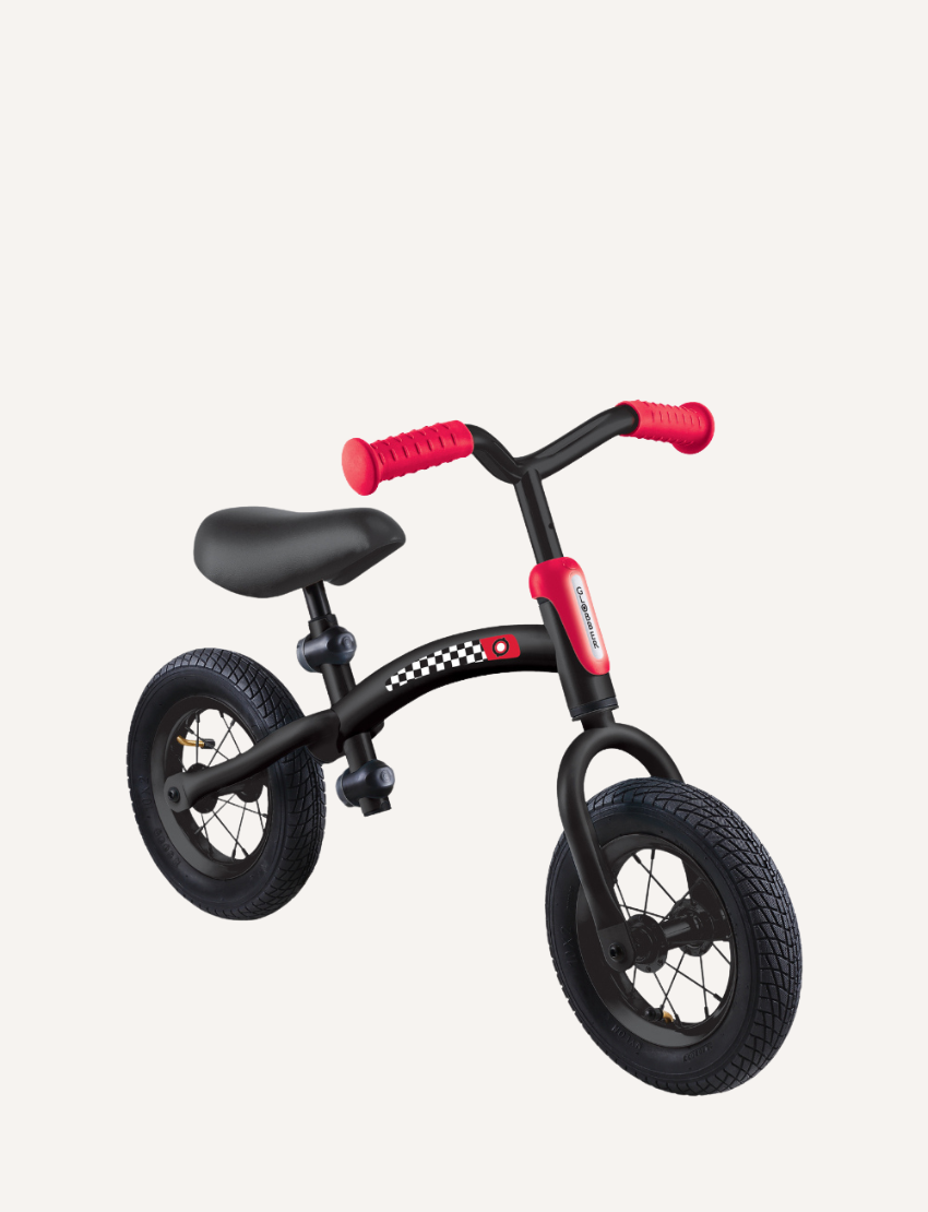 The Go Bike Air Balance Bike by Globber is a small, black balance bike featuring red handlebars and seat adjustments, specifically designed for toddlers aged 3-6. It includes two thick black tires and a checkered pattern on the frame near the seat. The bike has no pedals, aiding young children in learning balance and coordination while developing essential motor skills.