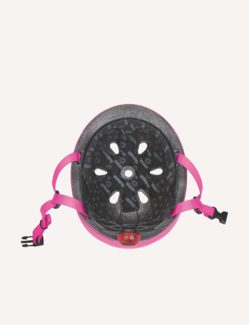 The Toddler Helmet with Flashing LED Light from Globber, available in XXS/XS (45-51cm), is shown from the inside. It features black foam padding with ventilation holes, adjustable pink straps with a buckle, and interior patterns and text for branding.