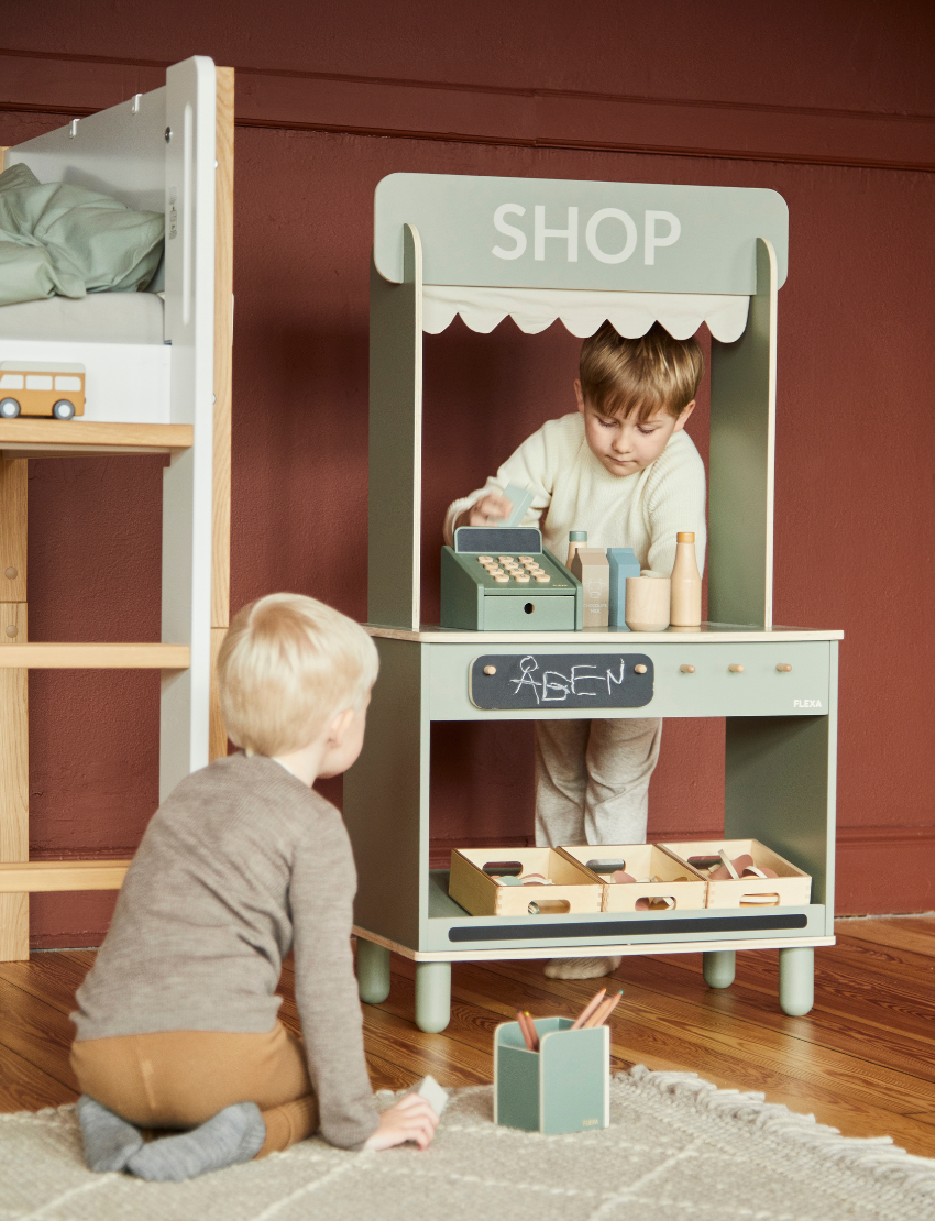 The Flexa Shop and Cafe is a grey play shop adorned with a "SHOP" sign above a charming scalloped awning. It features a counter, shelf, and knobs, measures 113.6 cm in height, 60 cm in width, 36.4 cm in depth, and stands on four short cylindrical legs.