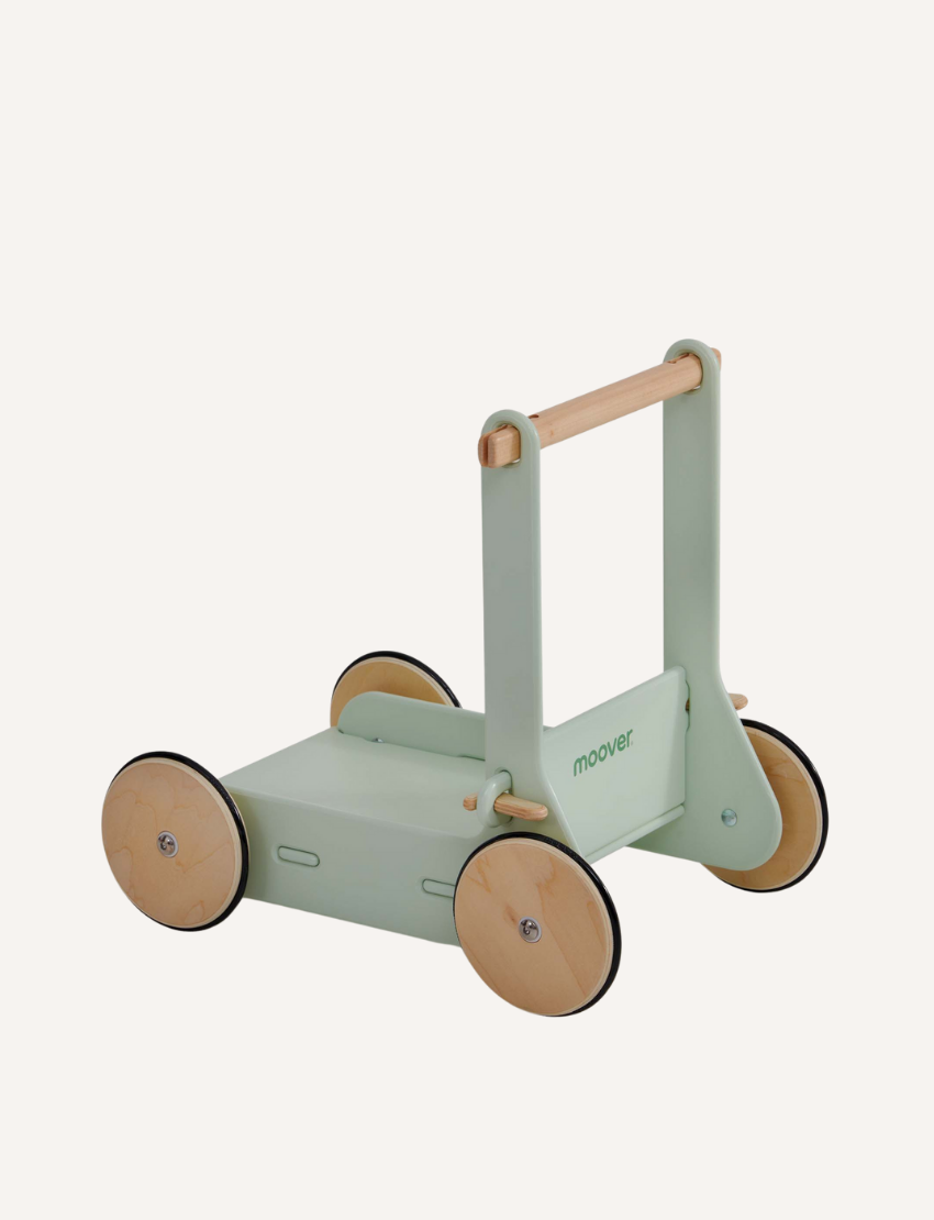 The Moover Toys Classic Baby Walker in green features a minimalistic design with "Moover" printed on the side. It has a wooden handlebar and four round wheels with a light wood finish and black rims.