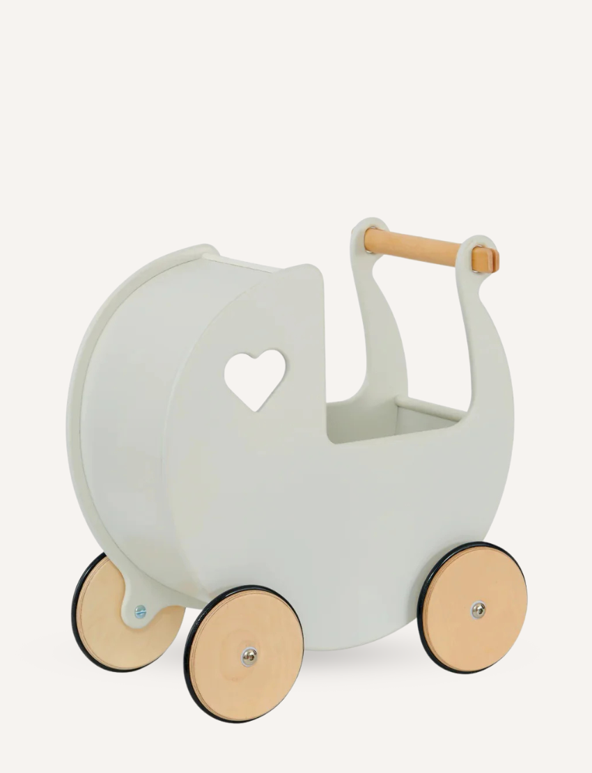 Two young children are playing with a Moover Classic Dolls Pram in off white. One child looks on while the other reaches inside. The pram features a heart-shaped cutout and large wooden wheels, and they play on a woven rug.