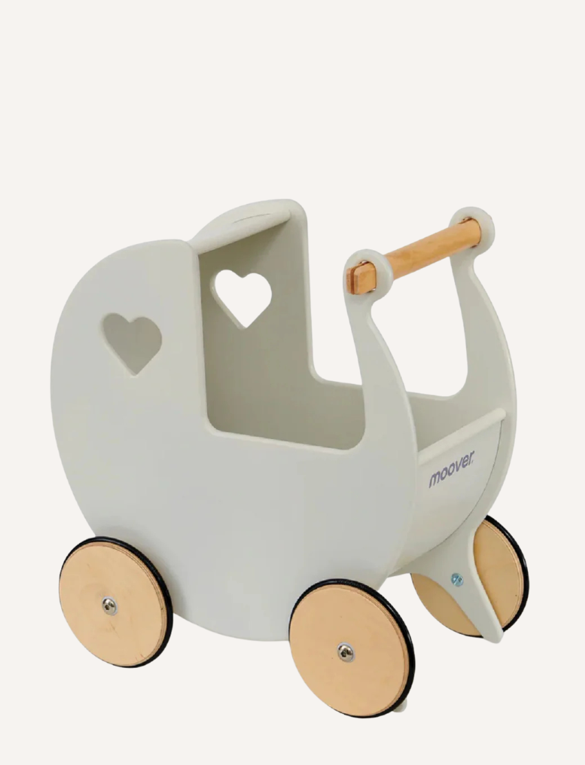 Two young children are playing with a Moover Classic Dolls Pram in off white. One child looks on while the other reaches inside. The pram features a heart-shaped cutout and large wooden wheels, and they play on a woven rug.