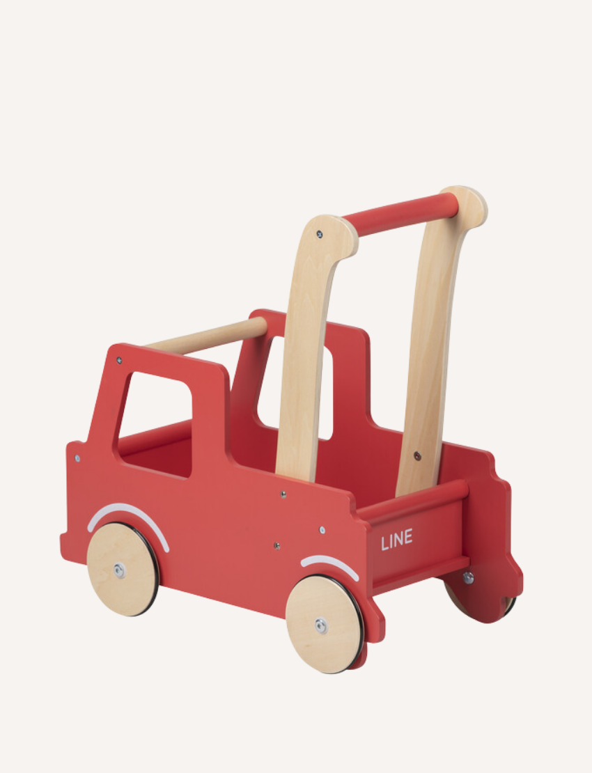 The Moover Push Truck is a red wooden toy car featuring beige wheels and handlebars. It boasts a simplistic design with cut-out windows and a small basket area at the back, marked with the word "LINE." This toy is designed for children to push or pull.