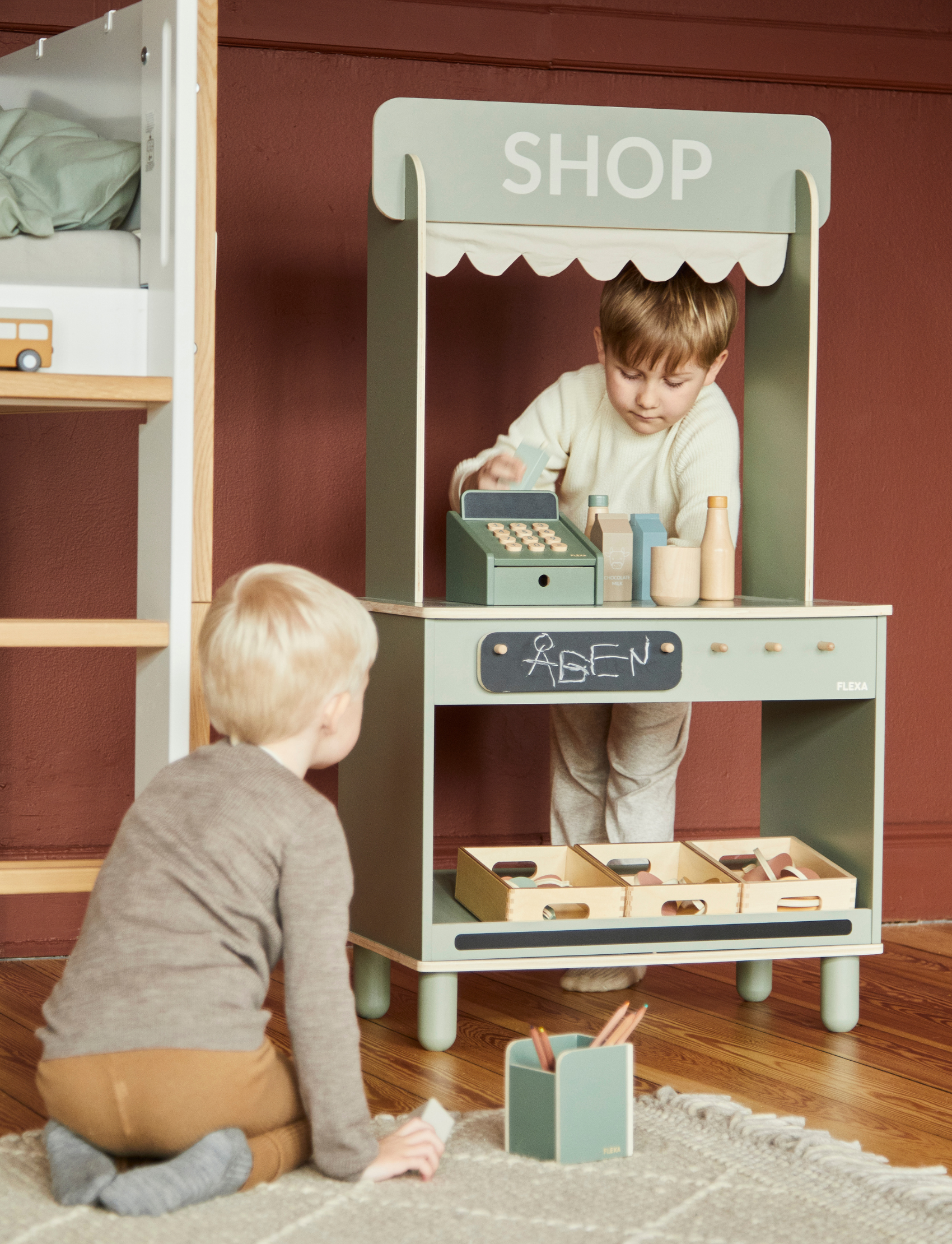 The Flexa Cash Register is a vibrant green wooden toy featuring wooden buttons and a display screen, ideal for imaginative play. It includes a numeric keypad with plus and minus symbols, along with wooden coins and a green card. The word "FLEXA" is elegantly displayed on both the register and the card.