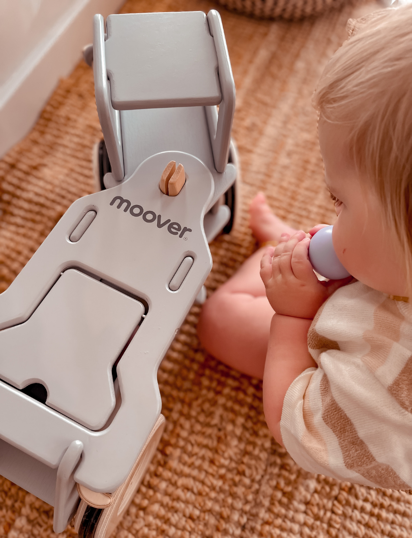 The Classic Dump Truck by Moover is a light gray wooden toy with smooth edges and large wheels, crafted using the Moover click system. Its simple design helps children develop gross motor skills, set against a plain white backdrop for minimalist appeal.