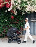 The Bumbleride ERA Pram features a green design, black frame, and brown handlebar. It offers air-filled tires with large rear and smaller front wheels for off-road use. An adjustable seat with a canopy and an under-seat storage basket complete this stroller's convenient features.