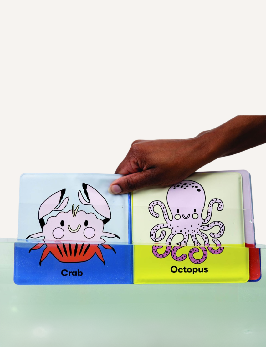 The image shows a children's book titled "Magic Bath Book - The Ocean" by Mudpuppy with the caption "Colors appear in water!" The blue cover features an illustrated fish with pink, yellow, white, and orange hues surrounded by bubbles. Experience bath time fun with color-changing pages!