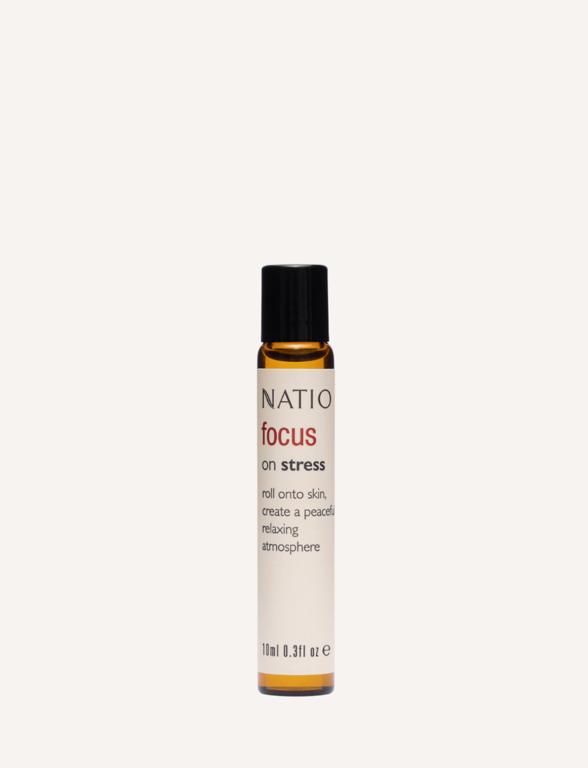 A small, cylindrical amber bottle with a black cap from Natio, labeled "Focus on Essential Oil Roll-On." The bottle features a roll-on applicator and text in English detailing the ingredients, usage instructions for skin nourishing benefits, and regulatory information.