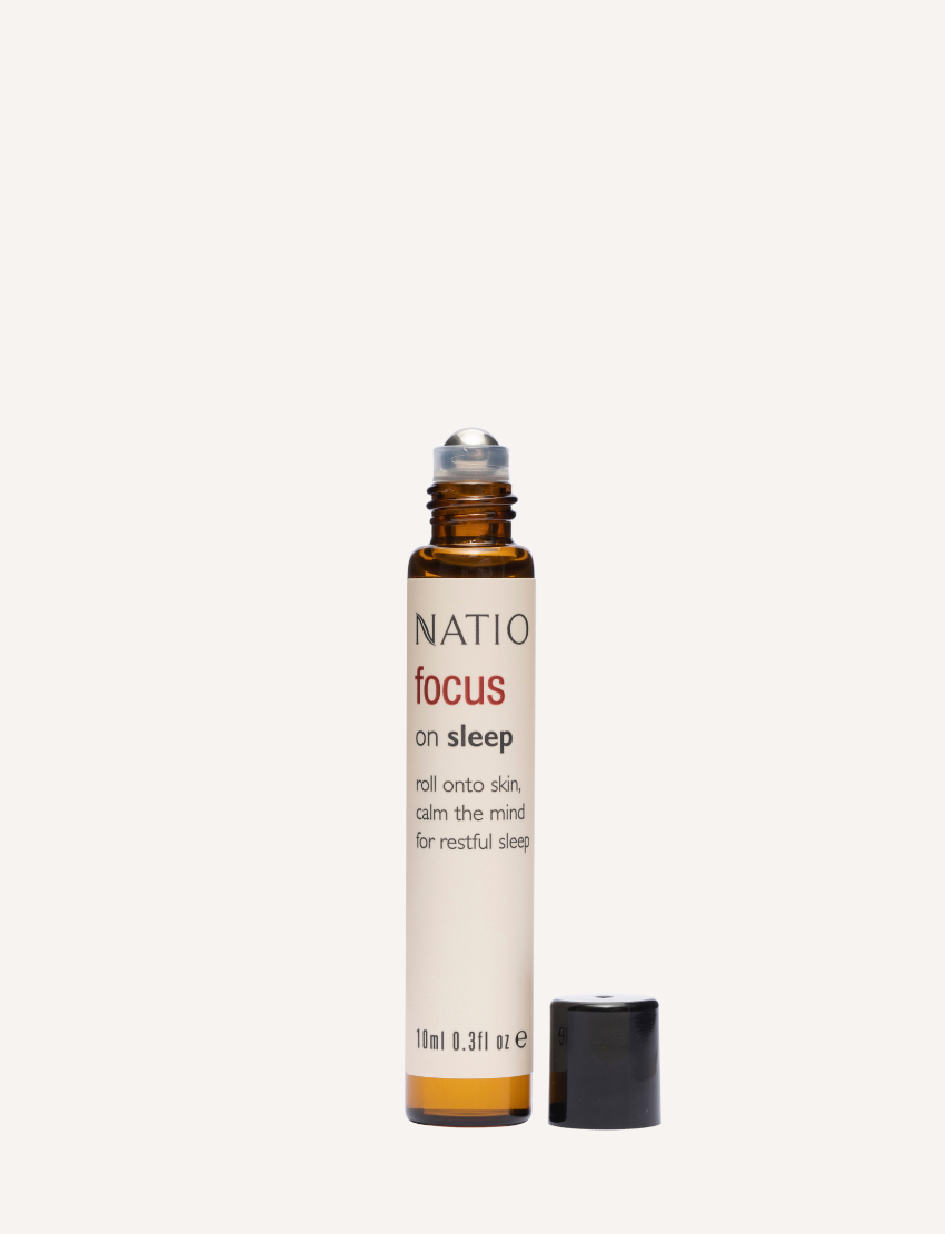 A small, cylindrical amber bottle with a black cap from Natio, labeled "Focus on Essential Oil Roll-On." The bottle features a roll-on applicator and text in English detailing the ingredients, usage instructions for skin nourishing benefits, and regulatory information.