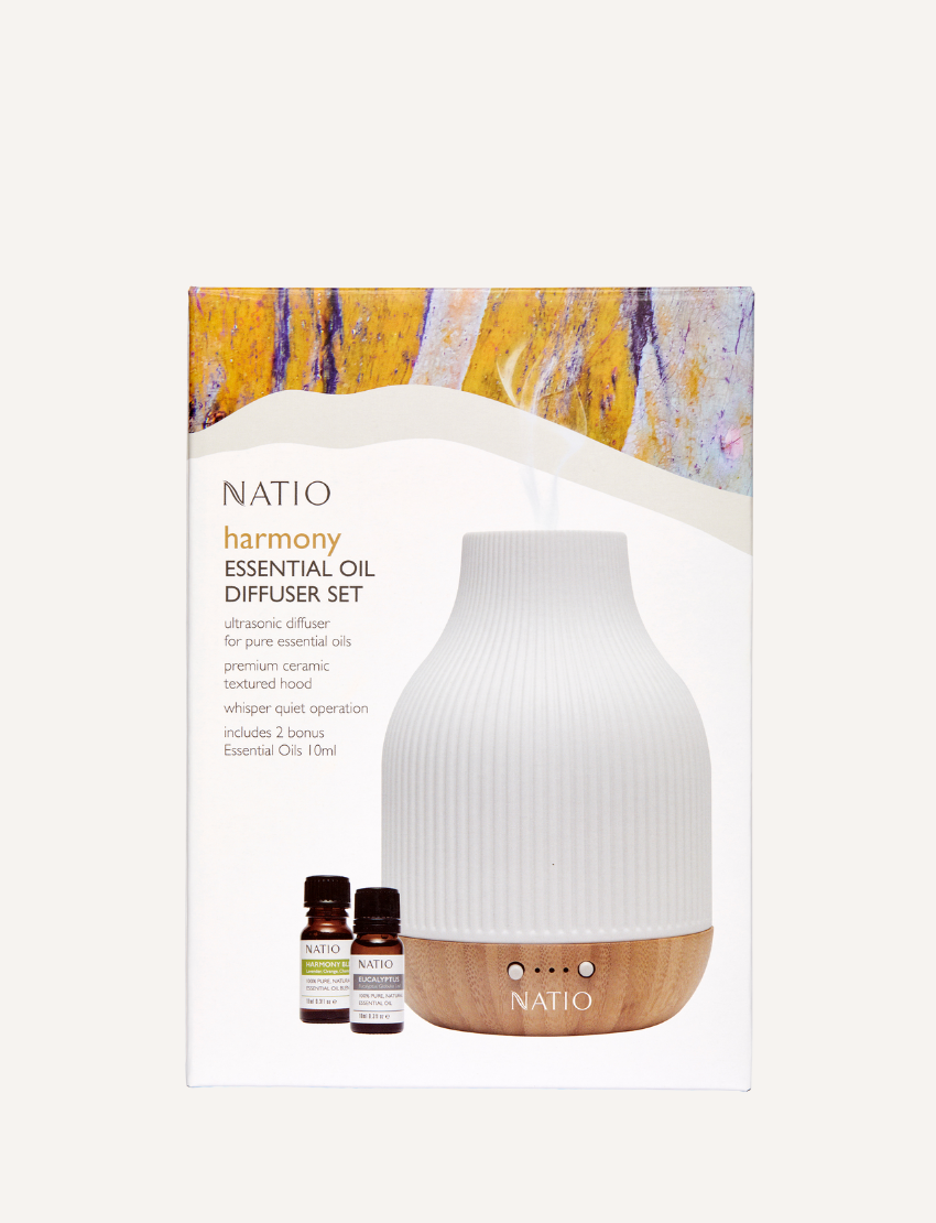 A white, ribbed Harmony Essential Oil Diffuser Gift Set from Natio, featuring a wooden base, is displayed next to two small bottles of essential oils labeled "Natio Eucalyptus" and "Natio Harmony" on a plain, neutral background. It promises a serene aromatherapy experience through advanced ultrasonic technology.