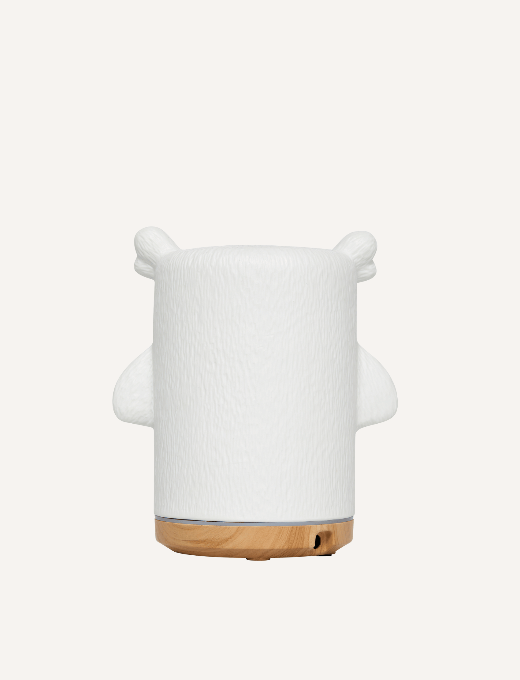 A white ceramic owl-shaped essential oil diffuser, ideal for children's aromatherapy, is placed next to its box. The box showcases "Natio Kids" along with an image and description of the diffuser. With its woodgrain-look base and charming owl design, the Kids Olive the Owl Ultrasonic Diffuser from Natio is perfect for any child's room.