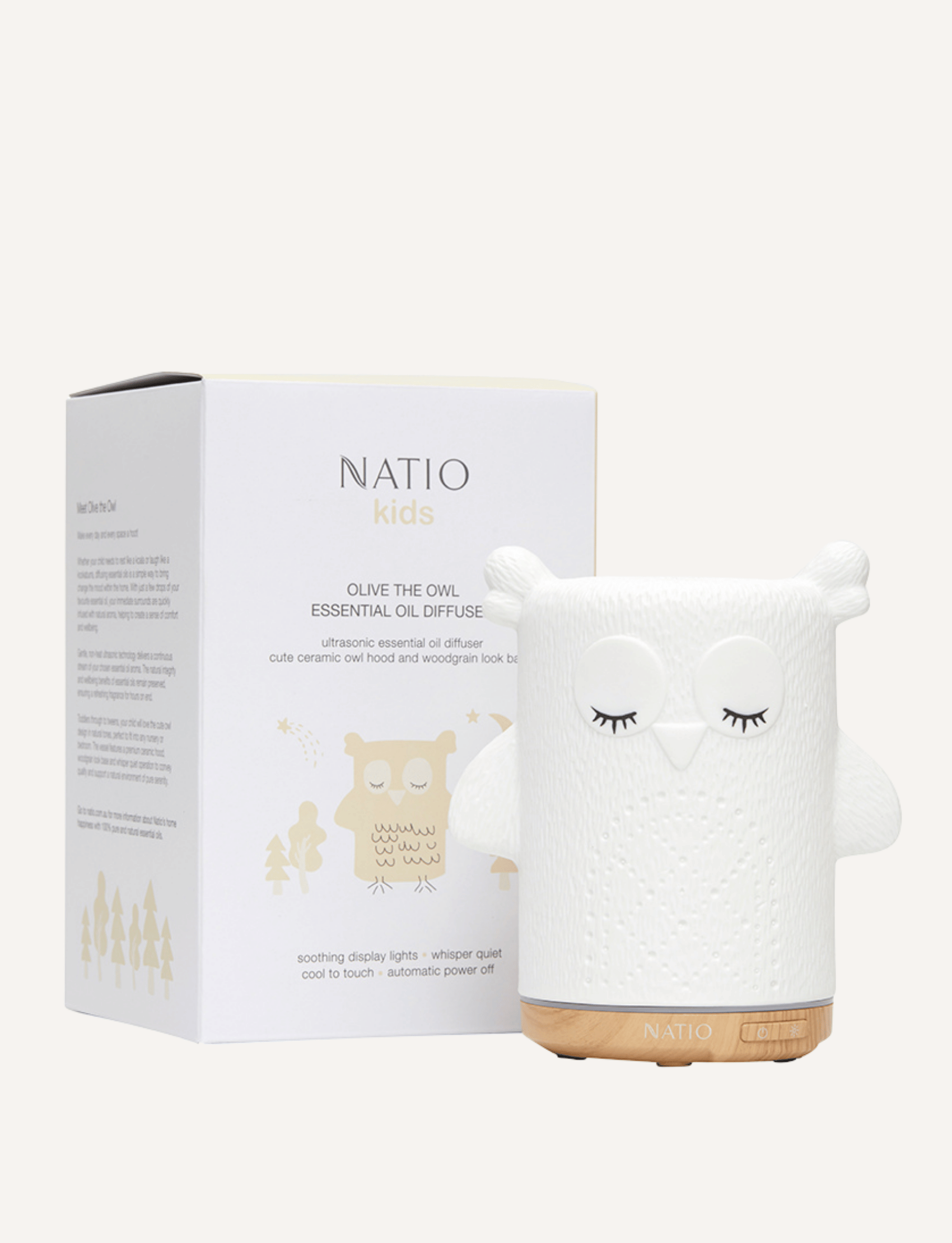 A white ceramic owl-shaped essential oil diffuser, ideal for children's aromatherapy, is placed next to its box. The box showcases "Natio Kids" along with an image and description of the diffuser. With its woodgrain-look base and charming owl design, the Kids Olive the Owl Ultrasonic Diffuser from Natio is perfect for any child's room.