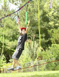 A product image of the Slackers Ropes Course set. Includes a box with the product image and label, three carabiners, two black straps, two red and black ratchets, and six colorful ropes with loops at the end for attaching to the line.