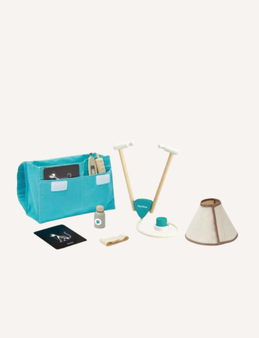 The image shows the Vet Set by PlanToys, complete with various toy tools and accessories. Items include a blue carrying case, a stethoscope, a cone collar, a bottle, a play syringe, a paw print card, and a small wooden plank.