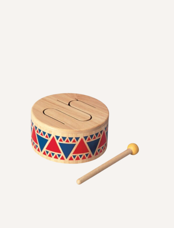 The PlanToys Solid Drum is a wooden percussion instrument adorned with red and blue triangular patterns around its circumference. It comes with a wooden mallet that has a yellow tip, all set against a plain white background.