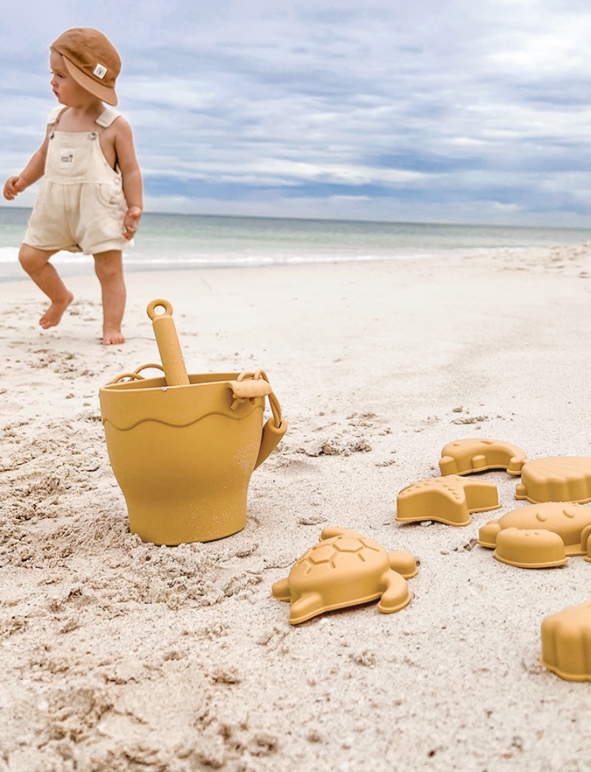 Playground's 8-Piece Bucket & Spade Set, featuring a yellow bucket with a handle, a small shovel, five sand molds in various shapes (sun, cloud, starfish, turtle, and crab), and a drawstring storage bag—all neatly arranged on a plain background.