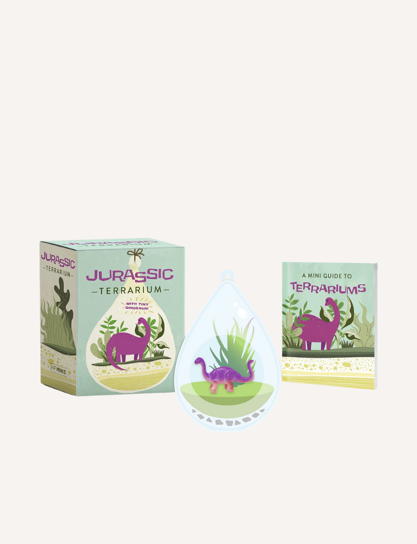 On display is the Jurassic Terrarium by Running Press, which includes a box adorned with a purple dinosaur illustration, a small plant terrarium, and a booklet titled "A Mini Guide to Terrariums," ideal for crafting your own miniature dinosaur habitat.