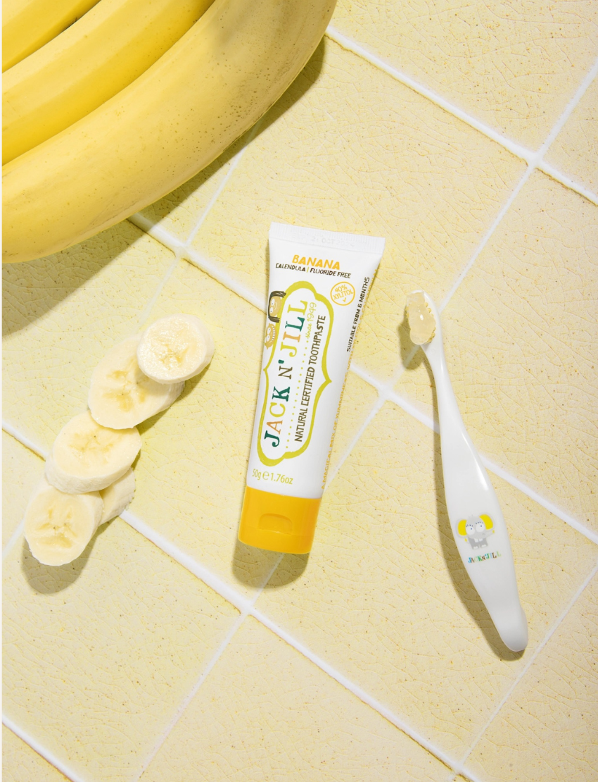 A 50g tube of Jack N' Jill Banana Toothpaste with a delightful natural banana flavor. The label highlights its Ecocert Certification and the fact that it is calendula and fluoride-free. Enriched with xylitol, the design showcases vibrant banana imagery.