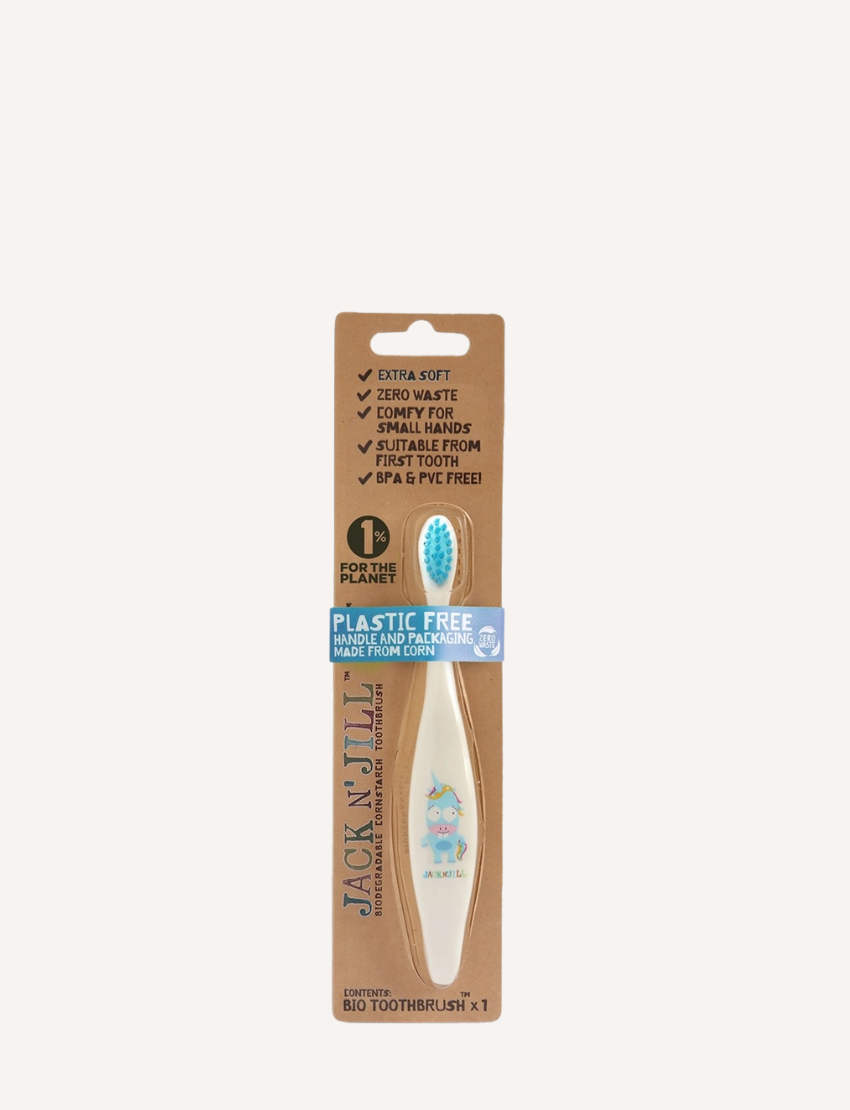 A Jack N' Jill Biodegradable Toothbrush, designed for children with a koala theme, and a tube of Jack N' Jill natural banana-flavored toothpaste adorned with cartoon animals on the label, are laid out on a gray surface.