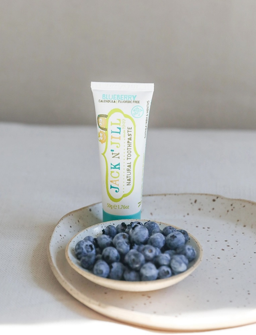 A tube of Jack N' Jill Blueberry Toothpaste, featuring a blueberry flavor, calendula, and no fluoride. The white packaging with green and blue accents includes cartoon characters for a fun brushing experience. This xylitol-infused toothpaste weighs 50g or 1.76oz.