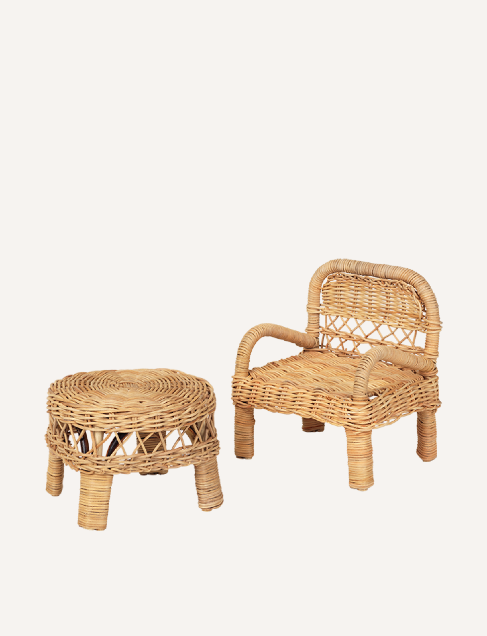 A Doll Chair - Rattan from Fabelab and a matching round wicker table are placed side by side against a plain background. The chair features a rounded backrest and armrests, while the table showcases a woven pattern on its sides. Ideal for an interior decorator seeking a nostalgic, retro look, both items are crafted from light-colored wicker.