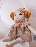 Doll Estelle, from the brand by Astrup, is a luxurious fabric doll with red hair. She is dressed in a floral outfit accented with a pink ruffled collar and comes placed next to a detachable pink tulle tutu and matching headband against a plain background. Perfect for imaginative play.