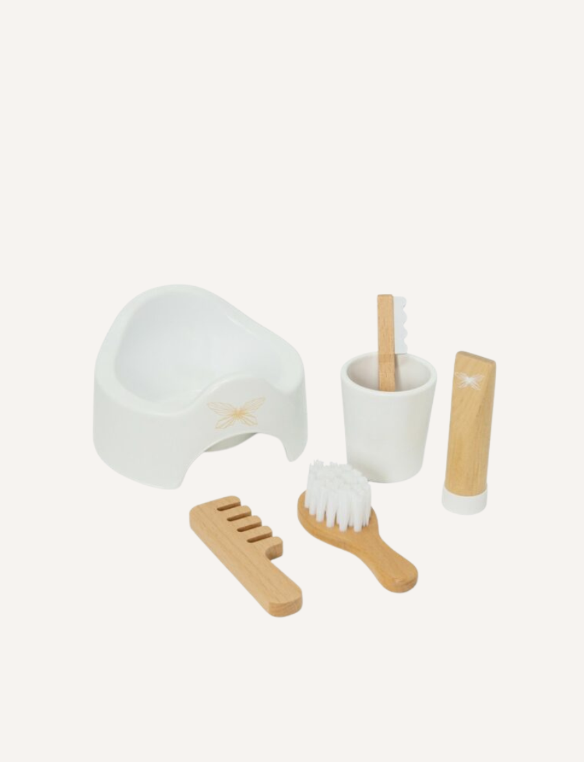 A Wooden Role Play Doll Nursery Set by Astrup, which features a white pot adorned with a butterfly design, a white cup containing a wooden toothbrush, alongside a wooden comb, a wooden hairbrush, and a white tube, all beautifully arranged on a white background.