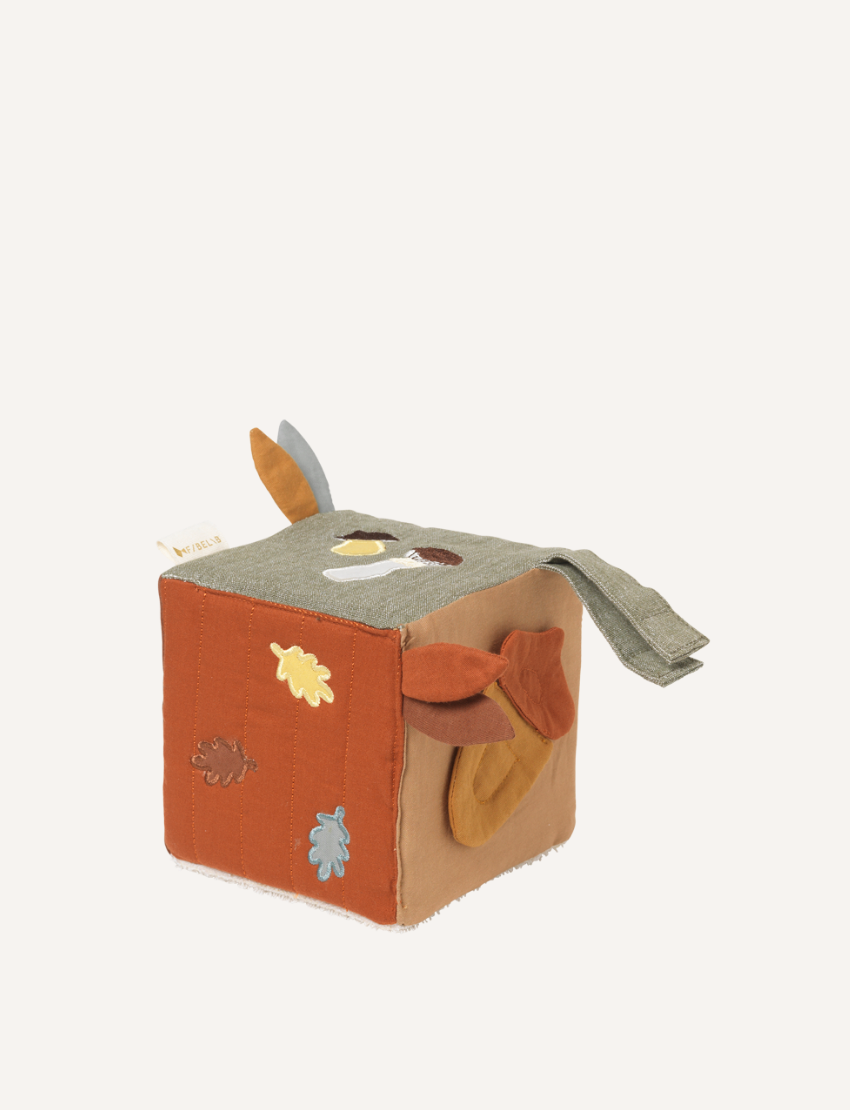 A soft fabric cube toy from Fabelab, featuring a hedgehog illustration on one side, a red and white mushroom on another, and a grey and orange fabric tag protruding from the top. The cube showcases a white, brown, and mustard color scheme with a label reading "Fabelab.