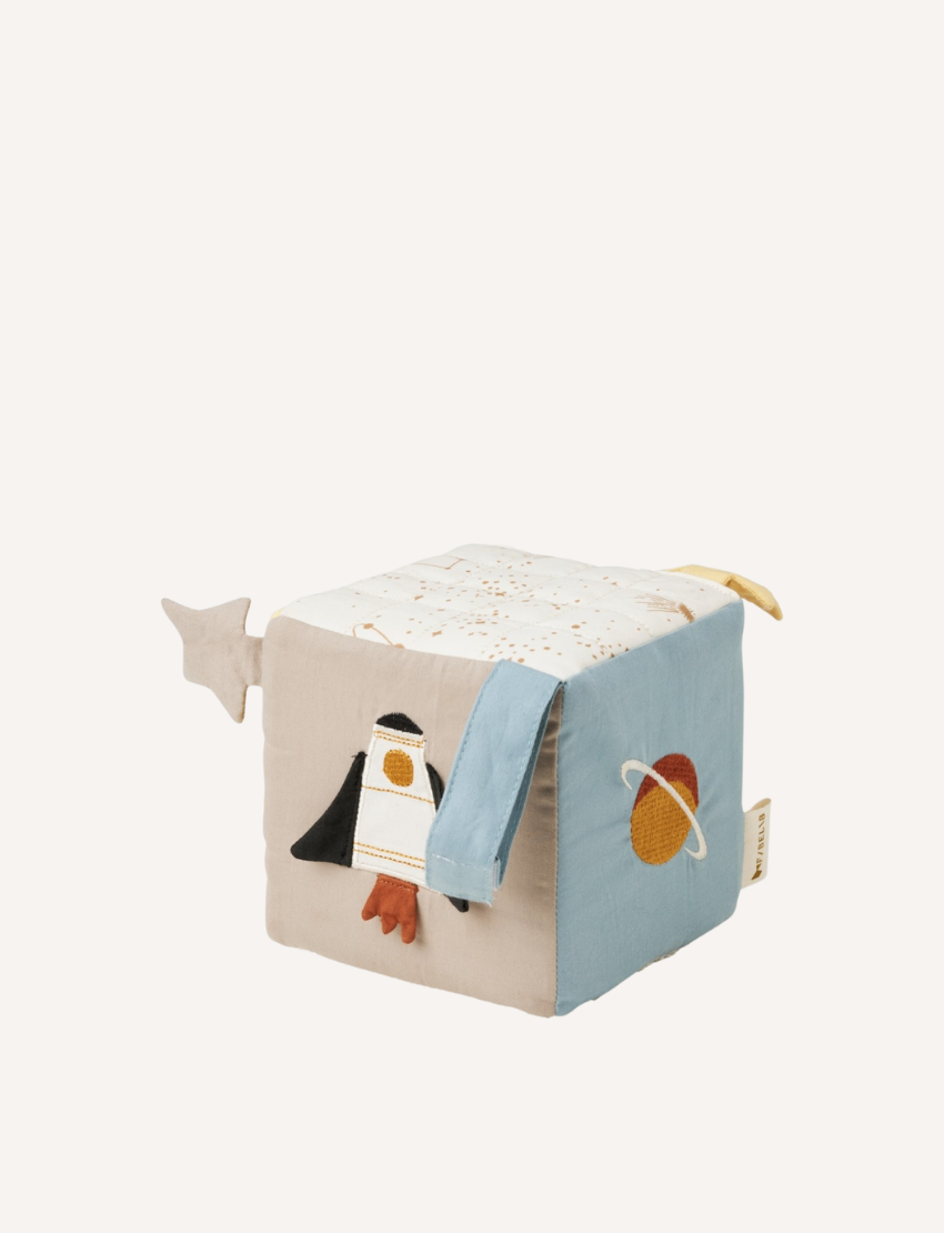 The Fabelab Fabric Cube is a soft, space-themed baby toy with designs of a rocket and planet. It features sensory-stimulating textures and embellishments, including a star-shaped tag, in calming blue, beige, and white hues—ideal as an on-the-go companion.