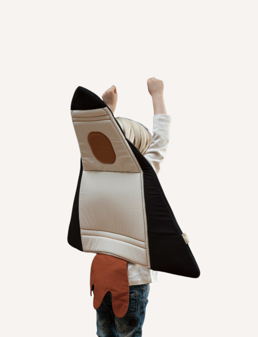 The Wings - Spaceship cape by Fabelab is a black fabric children’s cape with yellow straps on the front and a hood at the top. The bottom of the cape features orange fabric shaped like bursts or flames, giving it the appearance of a rocket launch.