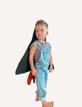 The Wings - Spaceship cape by Fabelab is a black fabric children’s cape with yellow straps on the front and a hood at the top. The bottom of the cape features orange fabric shaped like bursts or flames, giving it the appearance of a rocket launch.