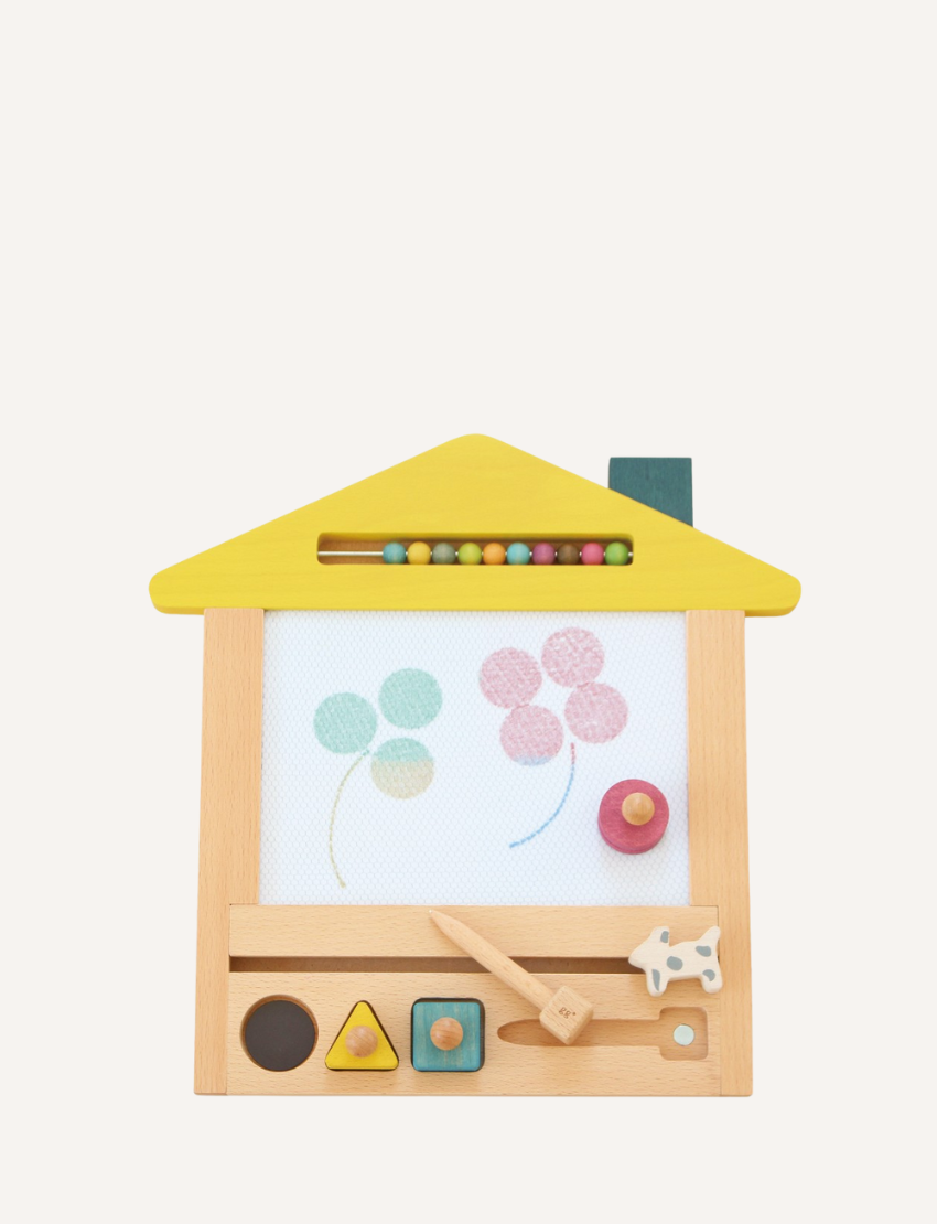 The kiko+ and gg* Magnetic Drawing Board is a wooden toy shaped like a house with a yellow roof. It features an abacus at the top, a wooden magnetic drawing board in the center adorned with flower shapes, and various colorful shapes and figures, including a cow at the bottom. This toy is perfect for imaginative play and enhancing motor skills.
