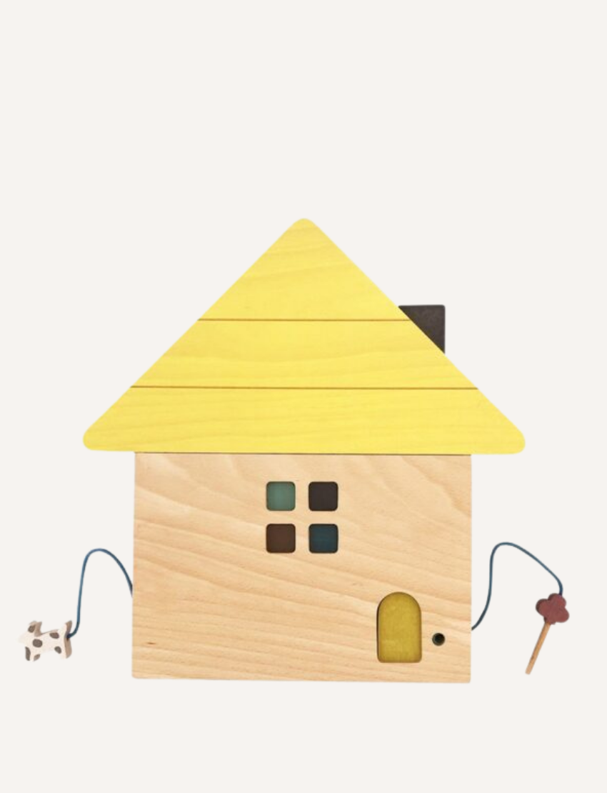 The Tsumiki House of Blocks by kiko+ and gg* features a delightful wooden toy house with a yellow roof. This charming house includes a small window with four panes, a rectangular door, and two strings—one ending in a small dog and the other in a tree. It comes as part of a 41-piece set.