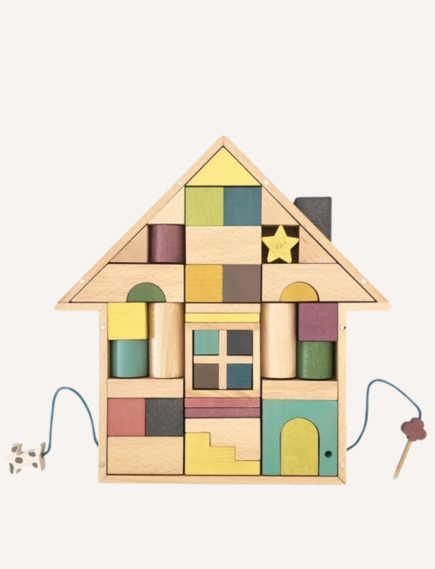 The Tsumiki House of Blocks by kiko+ and gg* features a delightful wooden toy house with a yellow roof. This charming house includes a small window with four panes, a rectangular door, and two strings—one ending in a small dog and the other in a tree. It comes as part of a 41-piece set.