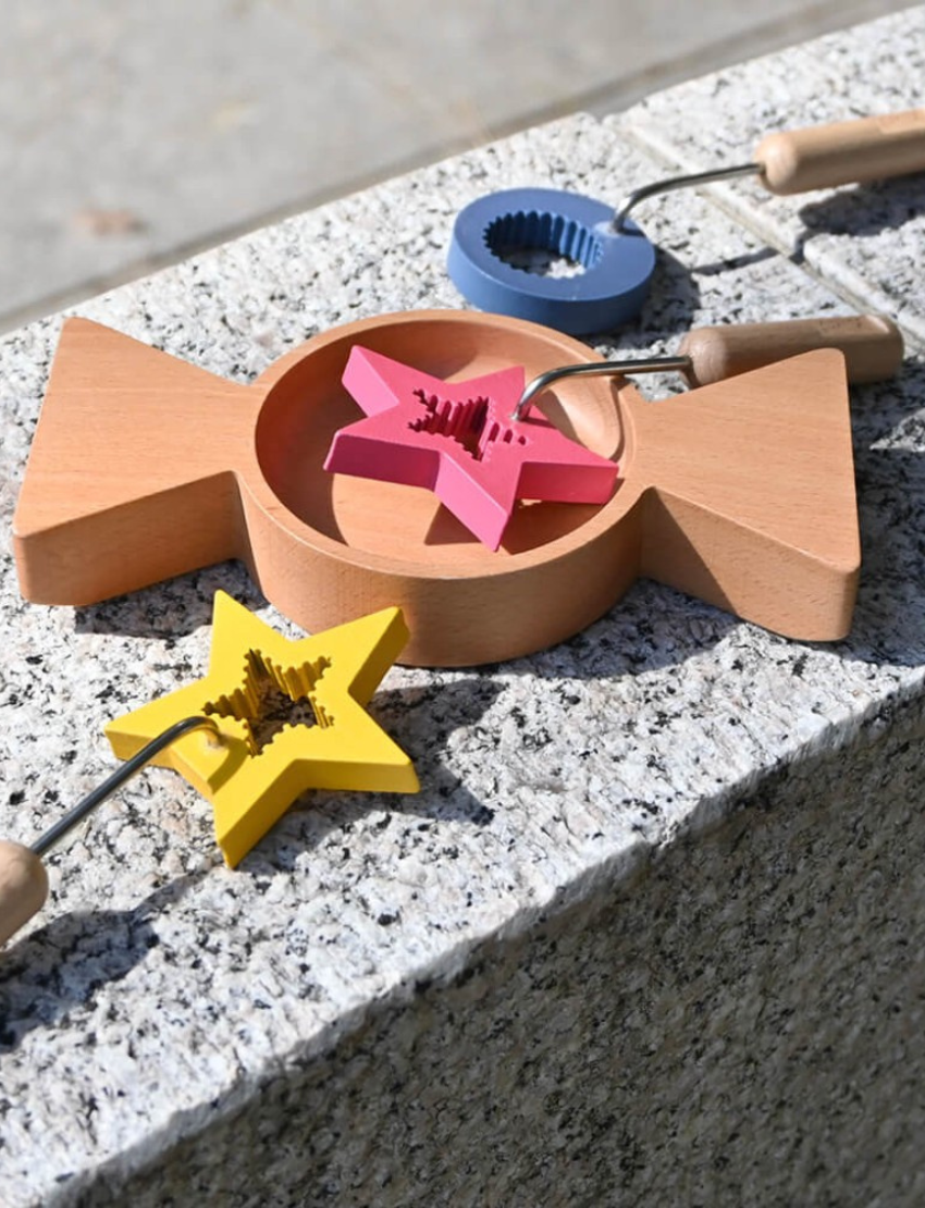 The image displays the Amechan Magical Bubble Wands by kiko+ and gg*, featuring three wooden wands and one wooden dish, ideal for eco-friendly bubble fun. The wands have star-shaped tops in red, yellow, and blue, with handles engraved "Kiko+." The circular dish includes two triangular extensions on opposite sides.