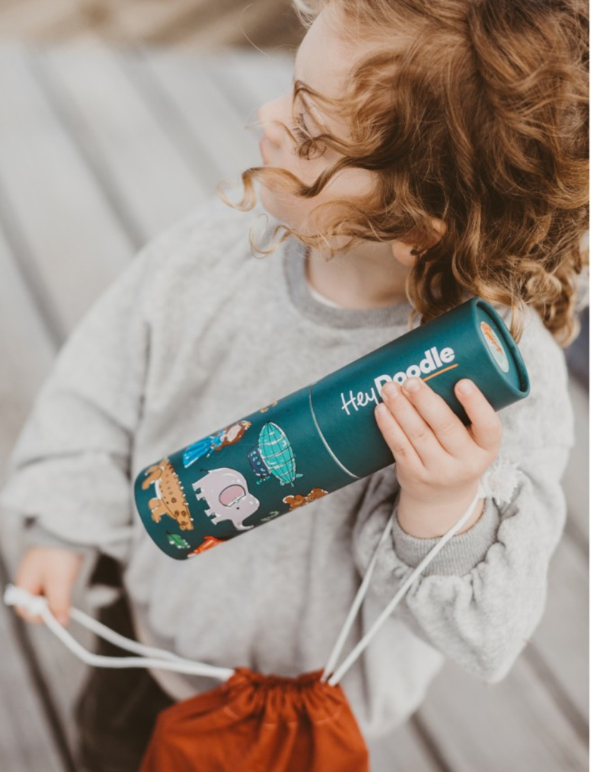 A cylindrical container labeled "HeyDoodle Mini Mat - ABC - Into The Wild" is next to a reusable drawing mat. The silicone mats feature illustrated animals like a whale, zebra, octopus, and giraffe, each paired with alphabet letters corresponding to their names.