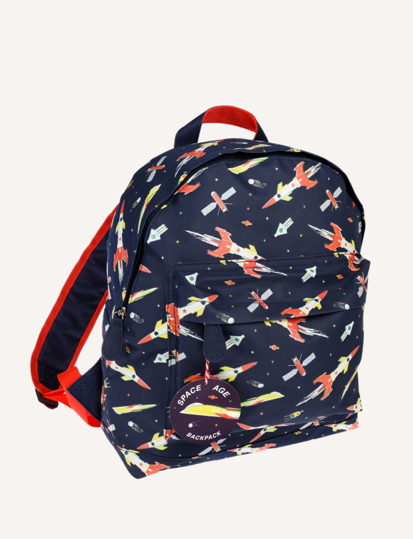 The Rex London Backpack, by Rex London, is a light blue children's bag featuring illustrations of dogs like pugs, dachshunds, and huskies. It’s ideal for school supplies with a front pocket and adjustable padded straps, plus a round tag on the zip.