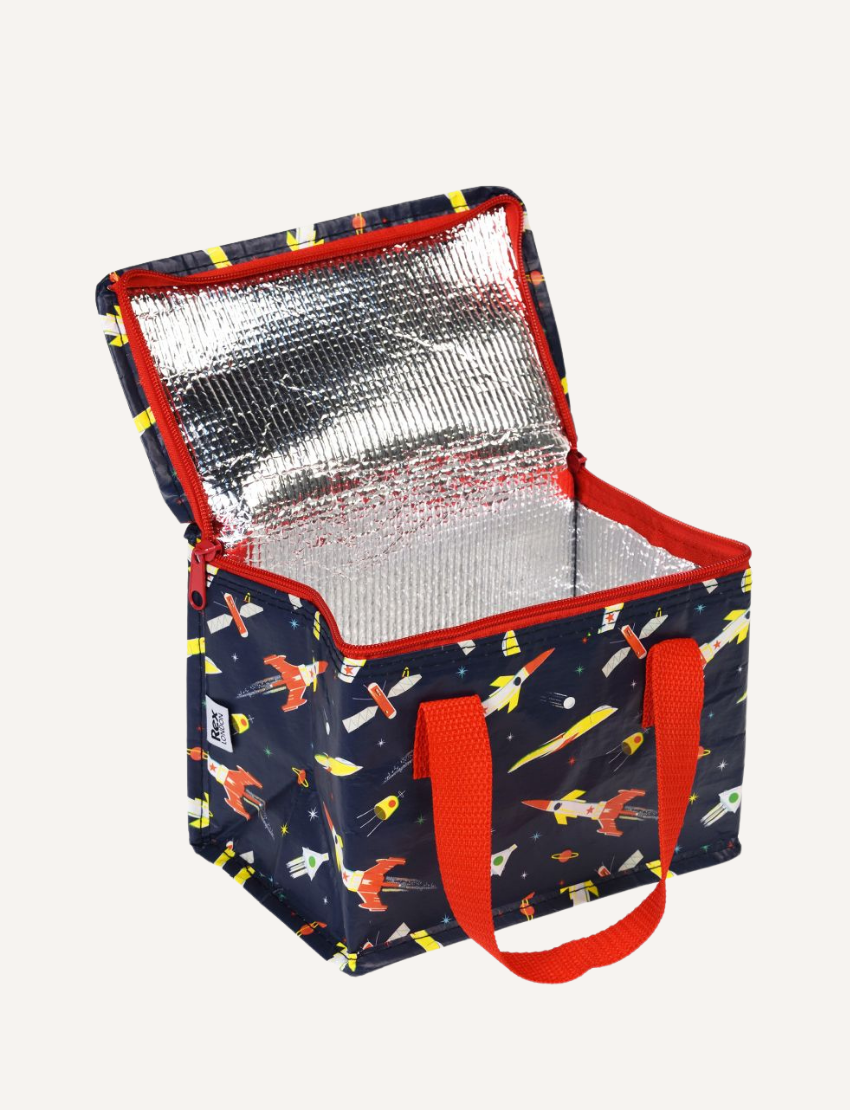 The Rex London Insulated Lunch Bag by Rex London showcases an open lid, revealing a reflective interior. It features a dark background adorned with vibrant rocket and spaceship illustrations, complemented by red zippers and handles.