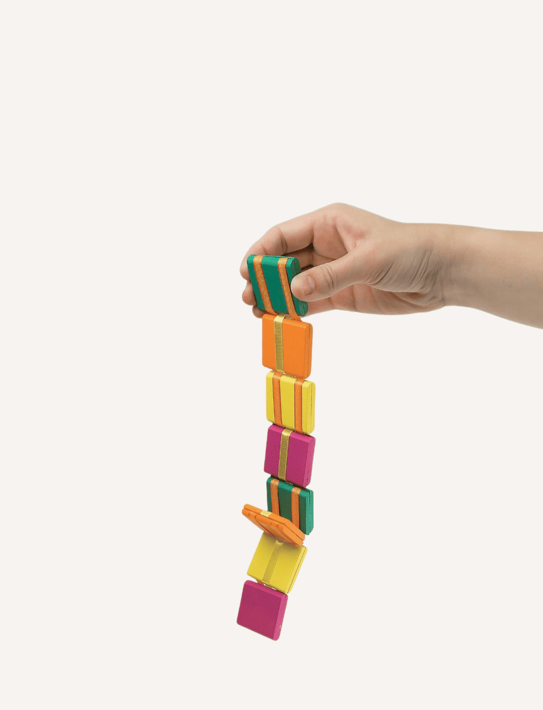 A hand holding a vibrant Sensory Genius "Jacobs Ladder" made up of connected rectangular blocks in orange, green, yellow, and pink. The blocks are arranged in a cascading manner, forming a flexible chain. This mesmerizing fidget toy stands out against the plain white background.