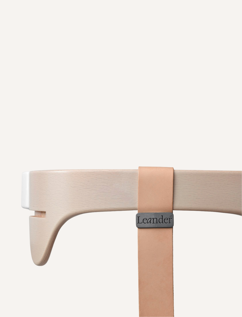 A close-up view of a beige wooden High Chair Safety Bar by Leander, featuring a leather strap. The item showcases clean, smooth lines and minimalist design, crafted in a white wash finish.