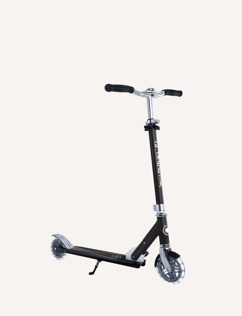 The Flow Element Scooter with Lights by Globber, featuring a sleek black and silver design, is shown. It has handlebars with black grips, a stand, and a rear brake. The scooter is positioned against a white background.