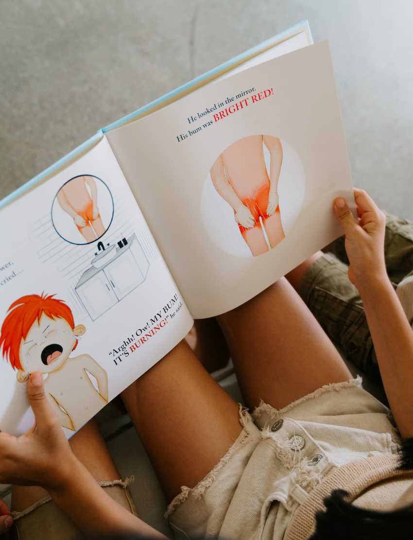 Three children are sitting on a couch, engaging with their Sensory Friendly Sunscreen Kit by The Play Way. The child in the middle is holding the kit, while the other two children are eagerly looking at it. All three appear focused on exploring the contents of the kit.