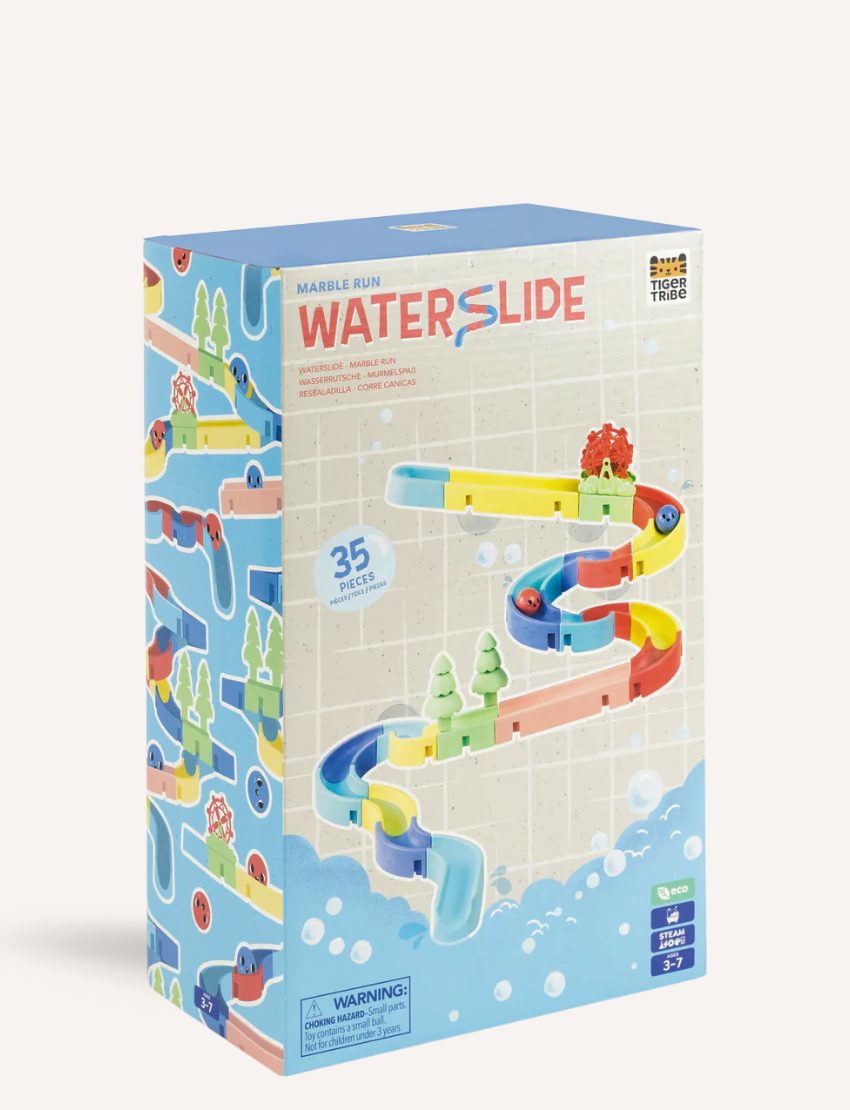 The Waterslide - Marble Run by Tiger Tribe features vibrant winding tracks in yellow, green, red, and blue with small green tree figures and a red spinning basket at the top. Blue and red marbles can be seen on the track.