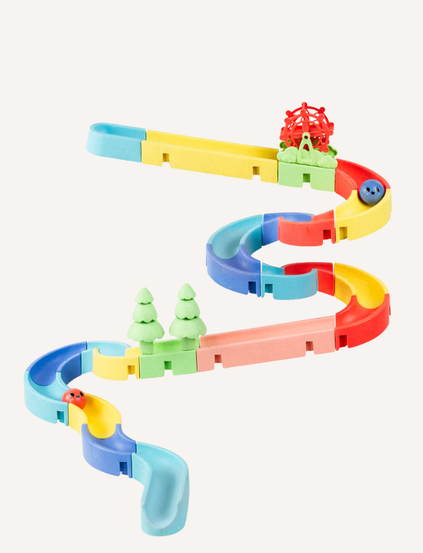 The Waterslide - Marble Run by Tiger Tribe features vibrant winding tracks in yellow, green, red, and blue with small green tree figures and a red spinning basket at the top. Blue and red marbles can be seen on the track.