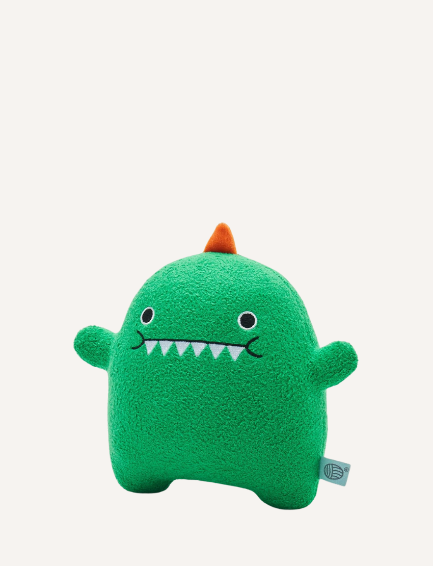 Green plush dinosaur toy with embroidered face, orange spikes, and a small brand tag.