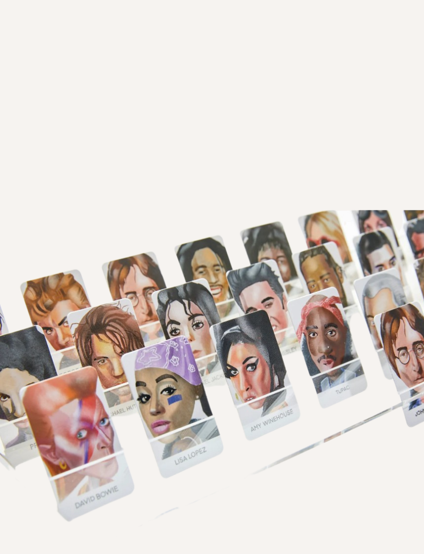 A close-up image of a "Guess the Musician Game" by Journey of Something, showcasing illustrated portraits of famous musicians from various genres and eras. The game pieces display multiple faces, such as those labeled "David Bowie" and "Tupac".