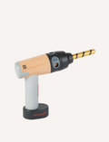 The BricoKids DIY Drill from Janod features a wooden handle and a grey plastic body. It comes with a gold toy drill bit and a silver toy screwdriver bit, both placed next to the drill. The brand name 