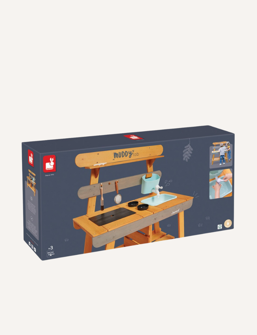 Janod's "Muddy Lab Outdoor Kitchen" is a boxed toy set that includes an outdoor wooden kitchen crafted from FSC certified wood. It features shelves, hooks for utensils, and an attached water dispenser. The packaging displays images of the assembled product alongside children joyfully playing with the Muddy Lab Outdoor Kitchen.